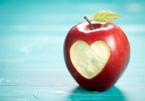 Apple with heart on turquoise table. On left side is empty space to put text or something else. This file is cleaned and retouched.